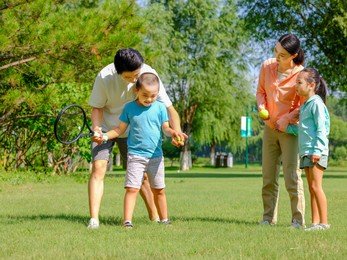 happy family of four playing tennis in the park high quality photo