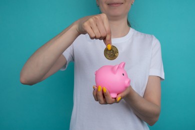 hand of elderly caucasian woman drops metal bitcoin coin into piggy bank pink pig on white background with place to place text