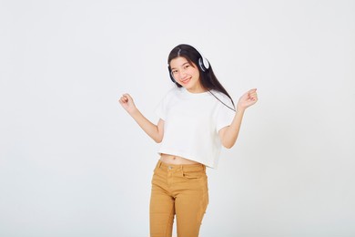 young asian woman with headphones and dancing on white background
