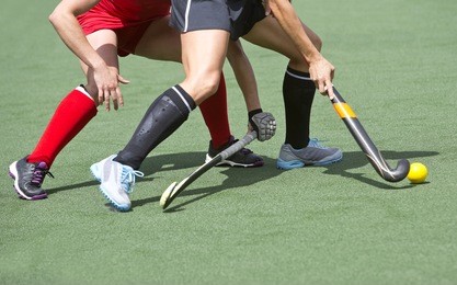 close up of two field hockey players, challenging eachother for the control and posession of the ball during an intense, competitive match on professional level