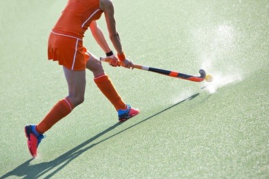 female field hockey player passing to a team mate on a modern, water artificial astroturf field