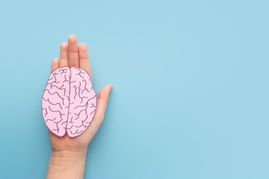 woman hands holding human brain shape made from paper on light blue background. awareness of alzheimer, parkinson's disease, dementia, stroke, seizure or mental health. neurology and psychology care.