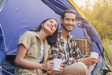 happy asian  young woman, girl and man drinking with mug of coffee, sitting in tent. adventure couple, people camping in forest. eco activity, lifestyle nature on holiday concept.