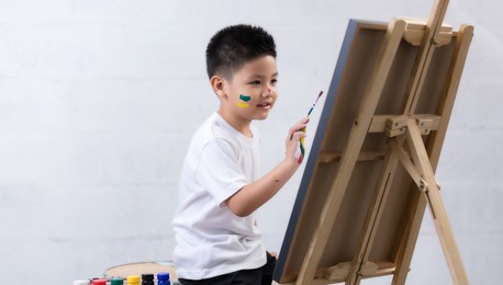 cute happy little asian boy painting with water color on canvas standing in white room at home, creative young artist at work. kids paint. children draw.