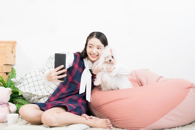 asian woman takes a selfie with a small dog. a woman takes a selfie as she holds her maltese dog.