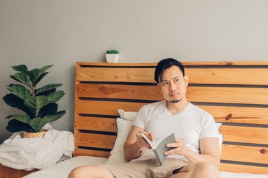 asian man is reading book on his bed in late afternoon.
