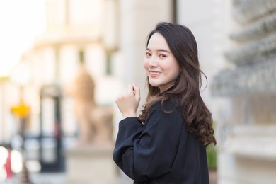 a picture of a beautiful long haired asian female in a black robe walking and looking out in the city outdoors.