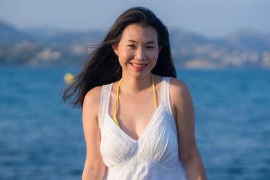 young happy and beautiful asian woman by the sea - attractive chinese girl in white dress enjoying relaxed summer holidays at tropical island in travel and lifestyle concept
