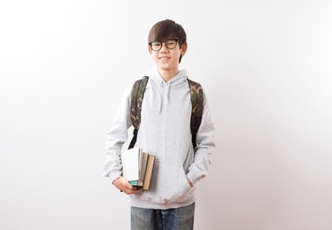 asian teen boy students carrying a backpack and books standing on white background.
