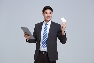 handsome and friendly face asian businessman smile in formal suit his using tablet and credit card on white background studio shot.	