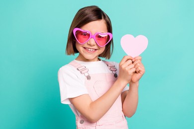 photo of funny adorable school girl wear pink overall glasses smiling holding little heart isolated teal color background