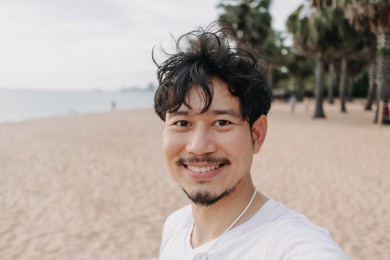 happy asian man take selfie with palm tree on the beach. summer travel concept.