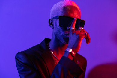 portrait photo of a dark-skinned guy with a beard. dressed in a black jacket and sunglasses. with metal ornaments on his hands purple and pink light