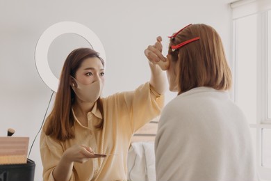 asian woman makeup artist is at work and wearing makeup on her model.