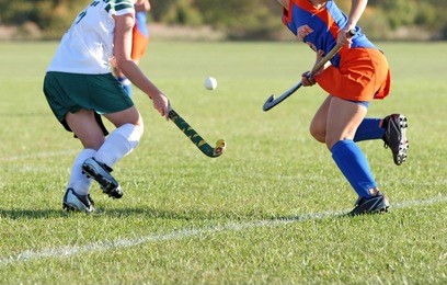 two girls battle for control of the ball in a field hockey game