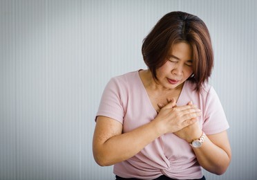 middle age asian woman sitting on bed suffering from sudden heart attack and hold chest. concept of emergency health care and affected from  cardiopulmonary resuscitation, heart problem.