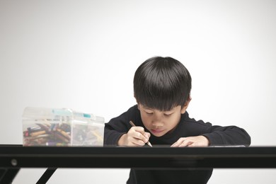asian boy about 5 years doing his homework, drawing and painting picture with color pencil.