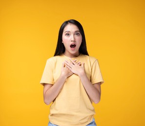young asian woman making hand gesture with surprise face. happy asian woman wearing yellow t-shirt standing over yellow background. portrait of happy asian female.