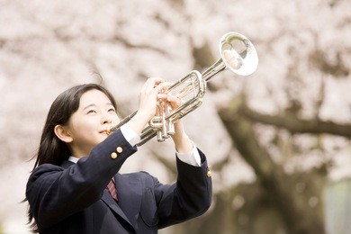 a middle school girl playing a trumpet under cherry blossoms
