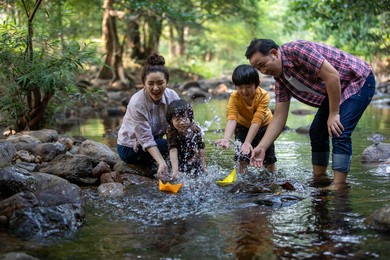 two son playing with paper boats at river ,asian family happy