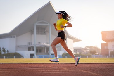 a young asian woman athlete runner jogging on running track in city stadium in the sunny morning to keep fitness and healthy lifestyle. young fitness woman runs on stadium track