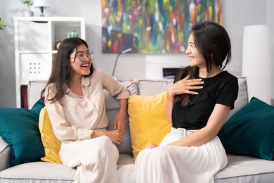 two pretty brunette friends hang out on the sofa in a modern apartment, roommates students, joke, tell funny stories, laugh, very good relationship, common topics, white smile