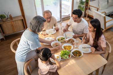 asian big happy family spend time have lunch on dinner table together. little kid daughter enjoy eating foods with father, mother and grandparents. multi-generation relationship and activity in house