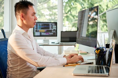 side view of programmer sitting at office desk and coding on computer