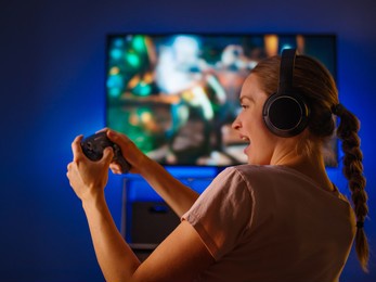 video games. online tournaments. game strategy. a young woman, a student, plays with friends remotely in an online game. she has a joystick in her hands, headphones on her head.