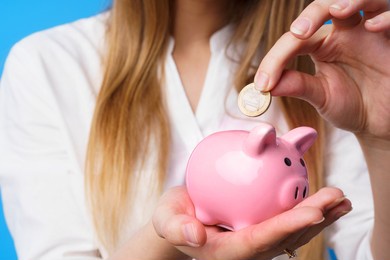 female putting money into pink piggy bank against blue background
