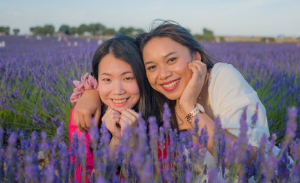 young happy and beautiful asian korean woman playing on lavender flowers field with her hispanic girlfriend enjoying sweet holidays together relaxed and carefree 
