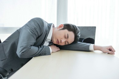 asian office worker sleeping on a desk with a laptop in the office building. the man is sleeping because of hard work.