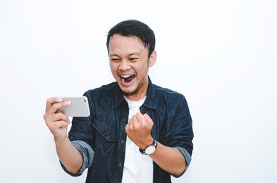 smile and happy face of young asian man when playing game at phone in hand.