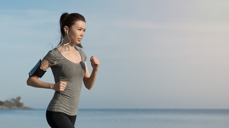 side view shot of female runner jogging outdoors on beach. mixed-race sportswoman jogger running in the morning, keeping her body in good shape, weightloss, dieting.