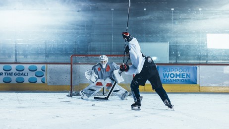 ice hockey rink arena: goalie is ready to defend score against forward player who shoots puck with stick. forwarder against goaltender one on one. tension moment in sport full of emotions.