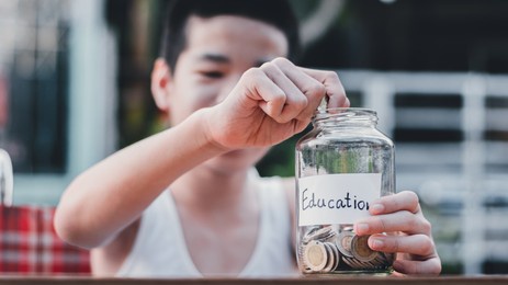 "education" text on a piggy bank with thai coins,blurred background of asian special need child on wheelchair saving money for education,learning in the future, happy disabled kid concept.