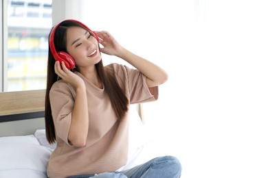 asian teen wearing headphones listening to music relax in bedroom, enjoy leisure weekend at home. stress free concept