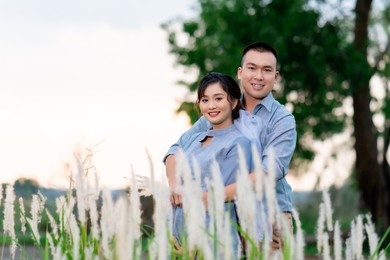 portrait of a handsome asian couple in the same color scheme jokingly posing for a photo together in a grass field at sunset in a beautiful golden glow