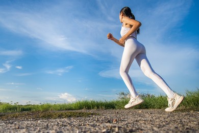beautiful asian women in sportswear running on green grass with blue sky in the background ready to exercise outdoor. healthy women concept. running workout.