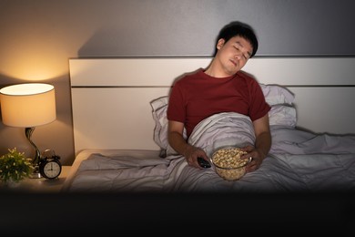 young man sleeping while watching tv on a bed at night