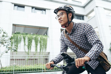 young man in glasses and helmet hurrying to work, he is riding on bicycle down the street