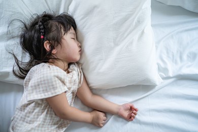 asian sleepy baby girl daughter lying down on bed in the early morning. adorable comfortable little kid take nap to rest and sleep alone in bedroom with blanket in house. children development concept 