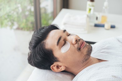 closeup face, asian man relaxation in spa salon with eye mask for under eye anti wrinkle. young male use smartphone in salon. facial face care men.