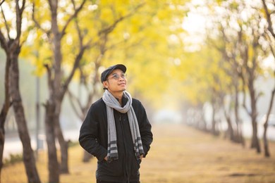 asian man wearing sweater while walking in the park under the yellow leaves ginkgo tree in autumn season