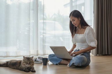 image of a young asian woman using a laptop at home with her pet.
