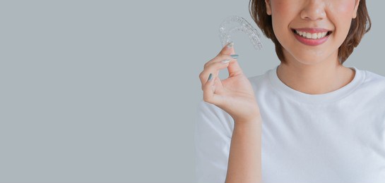 close up (isolated) young beautiful asian woman smiling with hand holding dental aligner retainer (invisible) on cream background of dental clinic for beautiful teeth treatment course concept