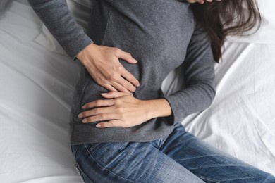 suffer from stomach ache. asian young woman sitting on the bed feeling pain in stomach.