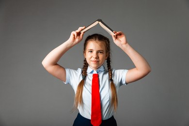 girl 12 years old in school uniform with book above head isolated on gray background