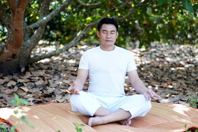  asian man in white custom sit and do meditation in forest.  soft and selective focus. blurred plants and trees.                                 