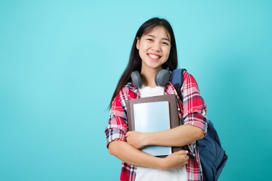 happy student. cheerful asian girl smiling to camera standing with backpack in studio over blue background. back to school concept.